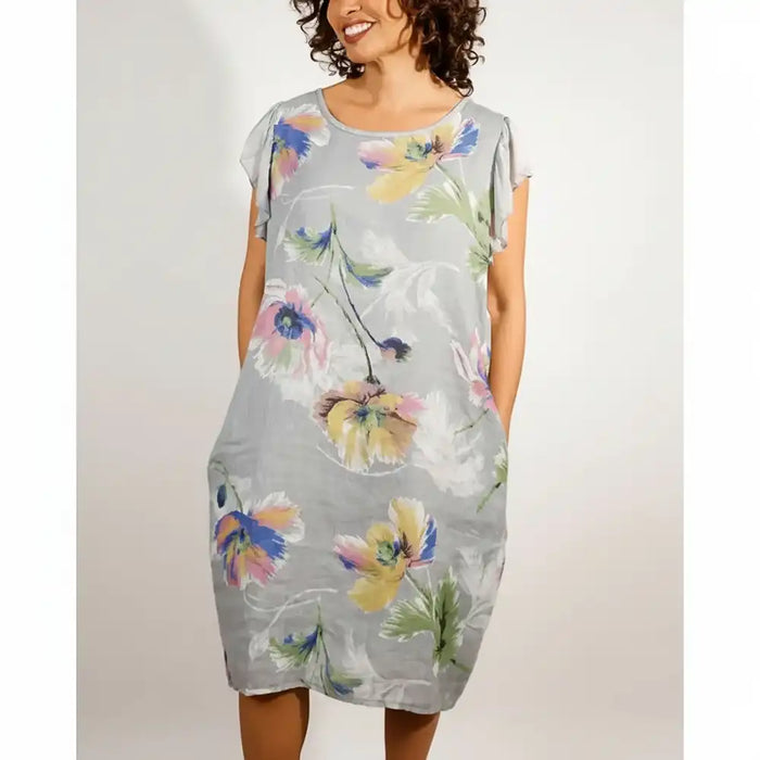 A woman wearing a light gray short-sleeve dress with a colorful floral print, standing against a plain light gray background.