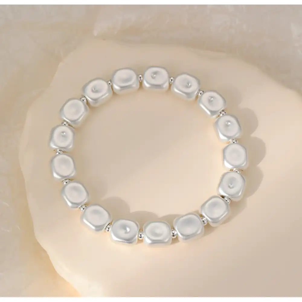 A stretch bracelet made of irregular, polished white stone-like beads separated by small silver spacer rings, displayed on a soft beige textured surface.