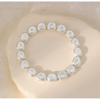 A stretch bracelet made of irregular, polished white stone-like beads separated by small silver spacer rings, displayed on a soft beige textured surface.