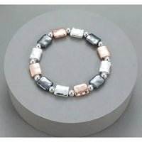 A stretch bracelet featuring alternating polished silver rectangular beads, silver round beads, and rose gold rectangular beads, displayed on a round gray pedestal.