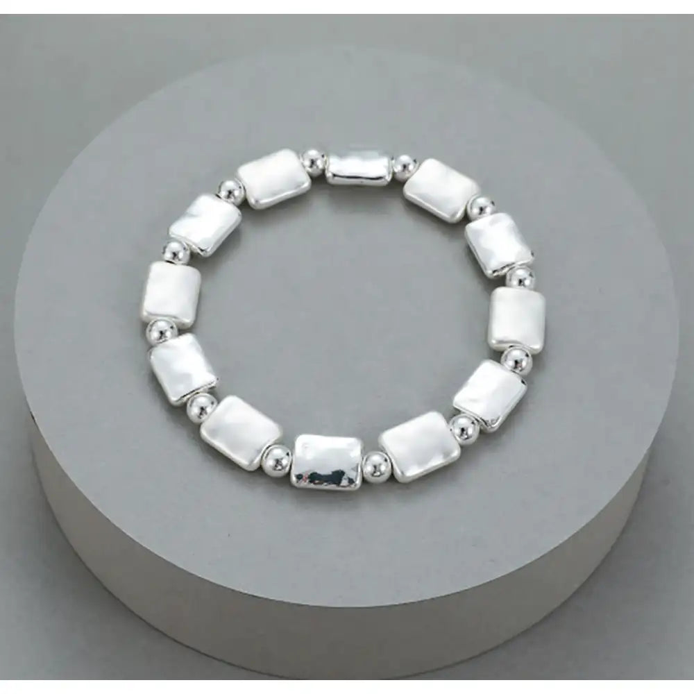 A sterling silver beaded stretch bracelet with rectangular and round beads, displayed on a round gray pedestal.