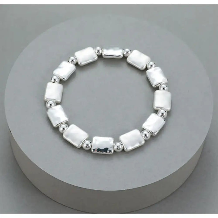A sterling silver beaded stretch bracelet with rectangular and round beads, displayed on a round gray pedestal.