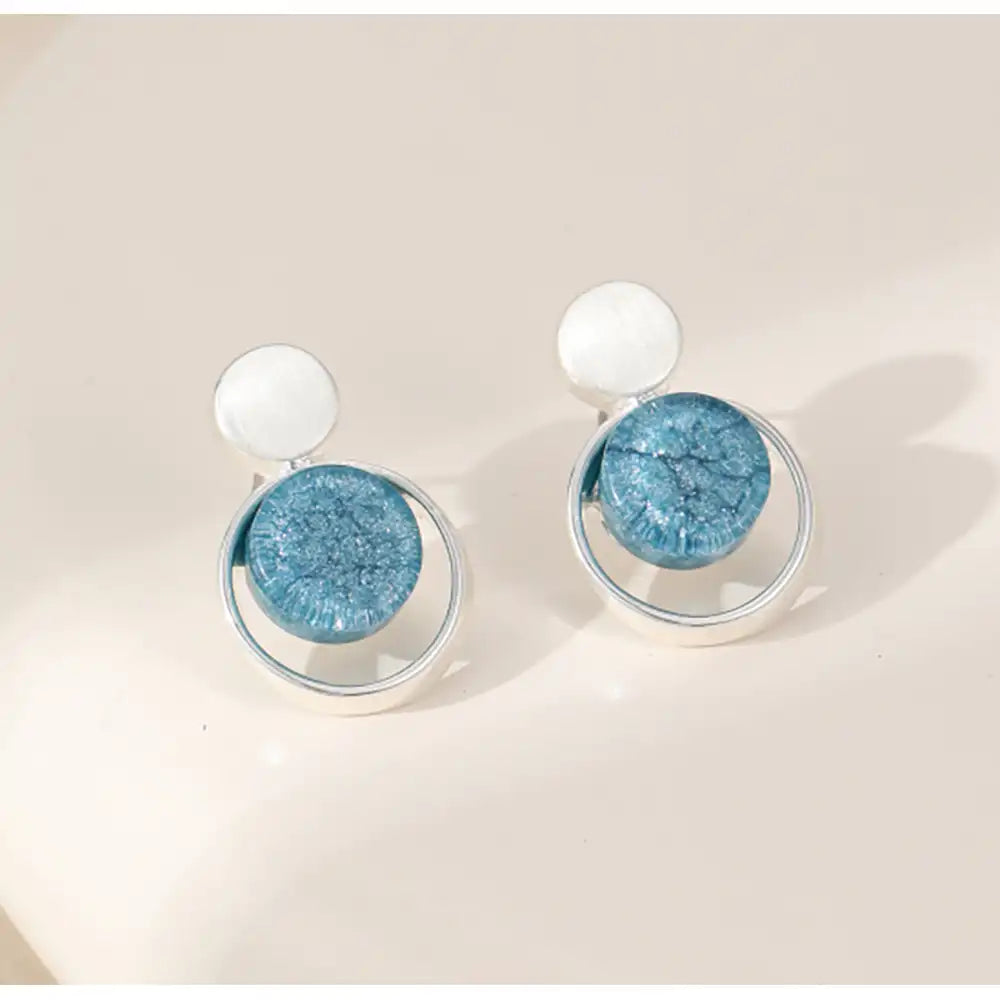 Pair of earrings with blue circular stones on a beige background