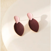A pair of drop earrings with a light pink teardrop-shaped top and a larger dark reddish-brown oval-shaped bottom, both outlined in gold-tone metal, displayed on a light beige surface.