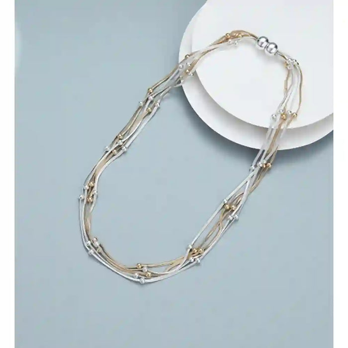 A multi-strand necklace with silver and gold-toned metal wires, decorative beads, and small geometric links, draped over a white plate on a light blue-gray background.