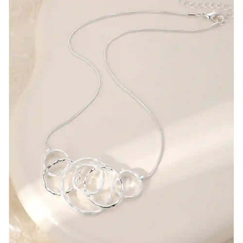 A silver chain necklace with a cluster of interlocking open circular rings, displayed on a light beige surface.