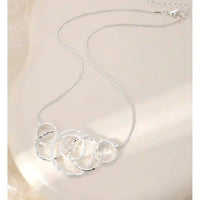 A silver chain necklace with a cluster of interlocking open circular rings, displayed on a light beige surface.