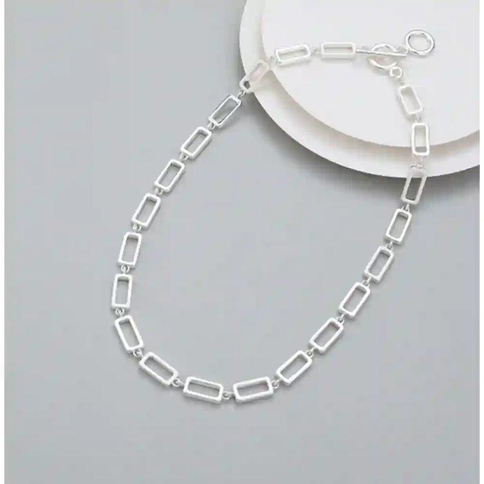 A silver rectangular link chain necklace displayed on a light gray background with a white plate prop.