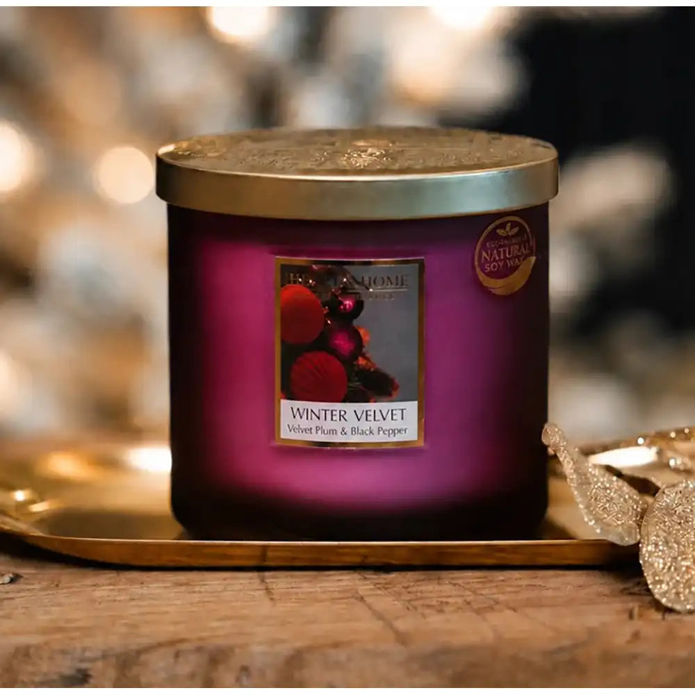 A purple scented candle in a glass jar with a gold lid, resting on a gold tray on a wooden surface. 