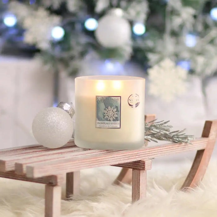 Candle with a snowflake design on a small wooden table in a festive setting.