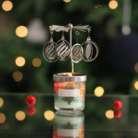 Candle with hanging silver ornaments against a blurred Christmas tree background