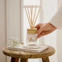 Hand holding a diffuser with wooden sticks on a small wooden table.