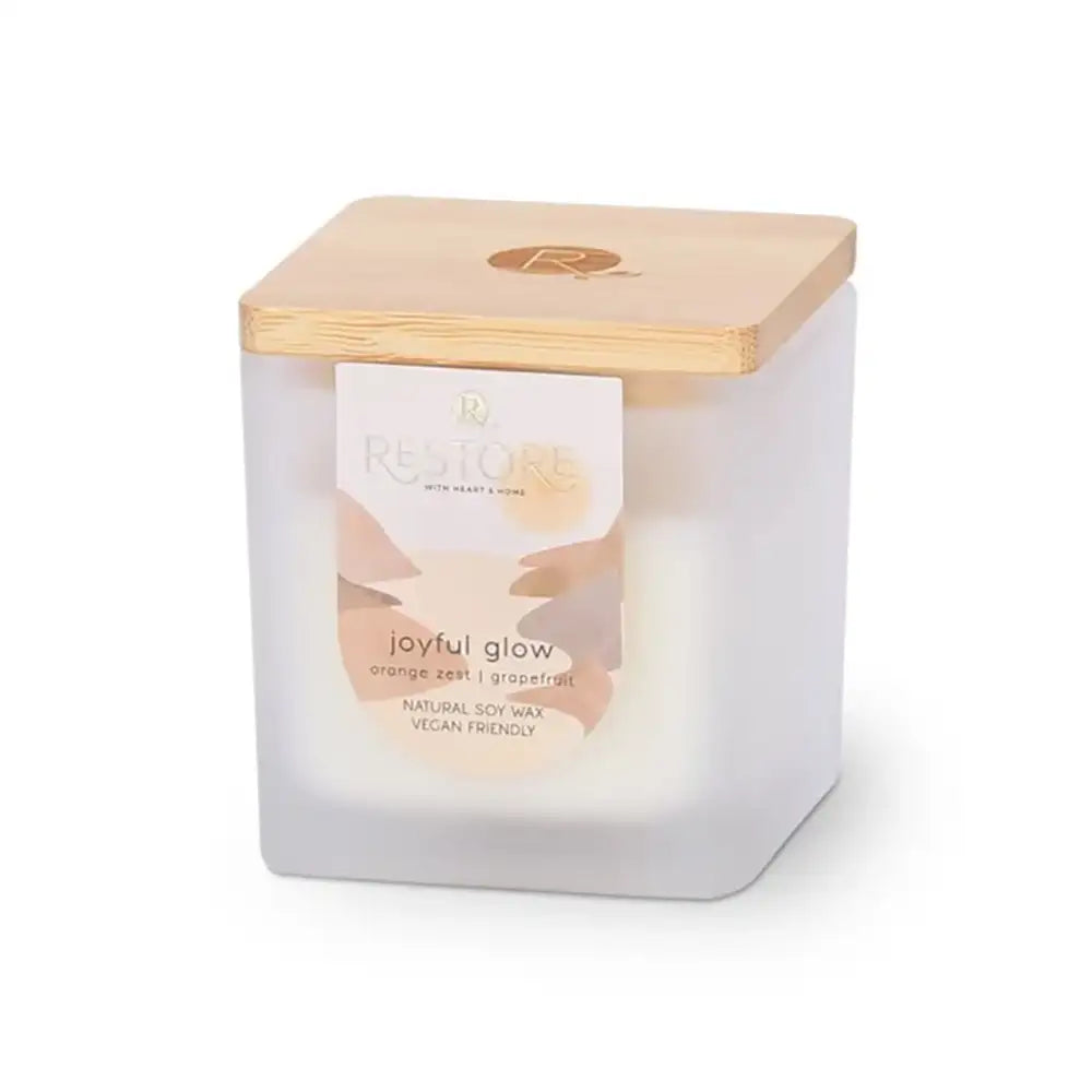 Candle with wooden lid labeled 'joyful glow' on a white background