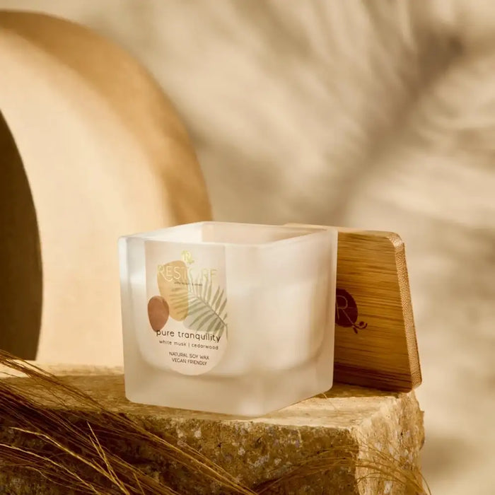 Frosted candle labeled 'Pure Tranquility' on a wooden stand with a soft, warm background.
