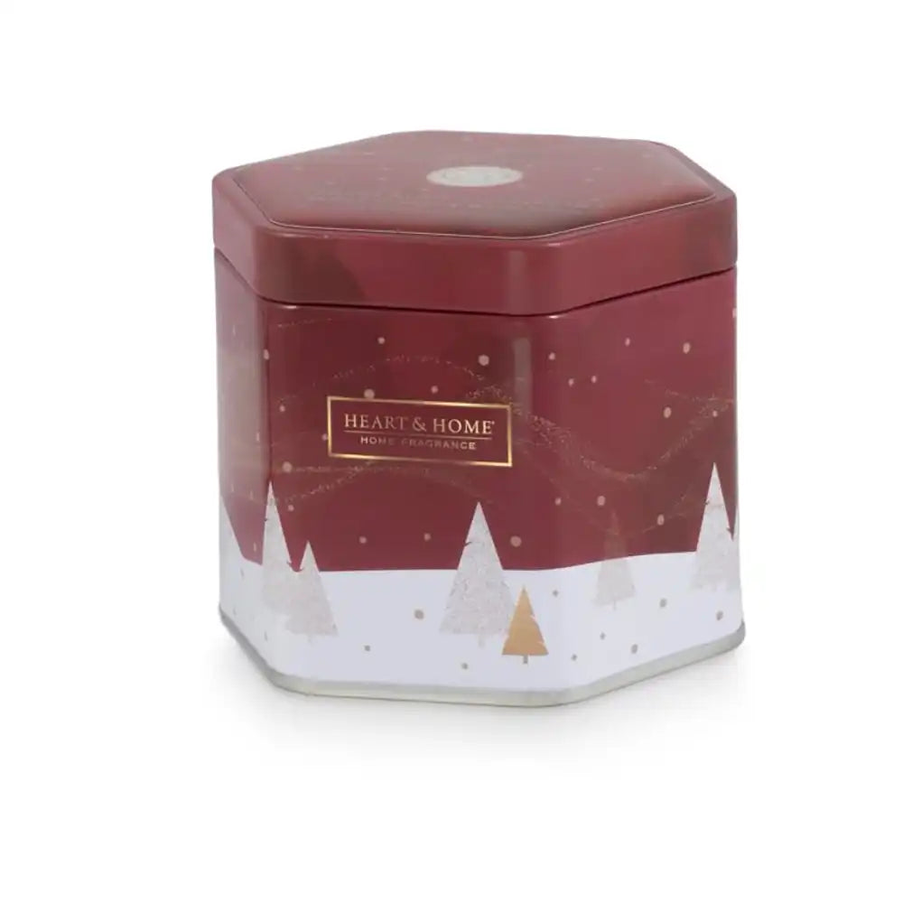 A hexagonal metal tin container for Heart & Home Melted Christmas Candle, featuring a deep red top half with subtle snowflake patterns, a white bottom half with minimalist gold and silver Christmas trees, and a gold brand label on the front.