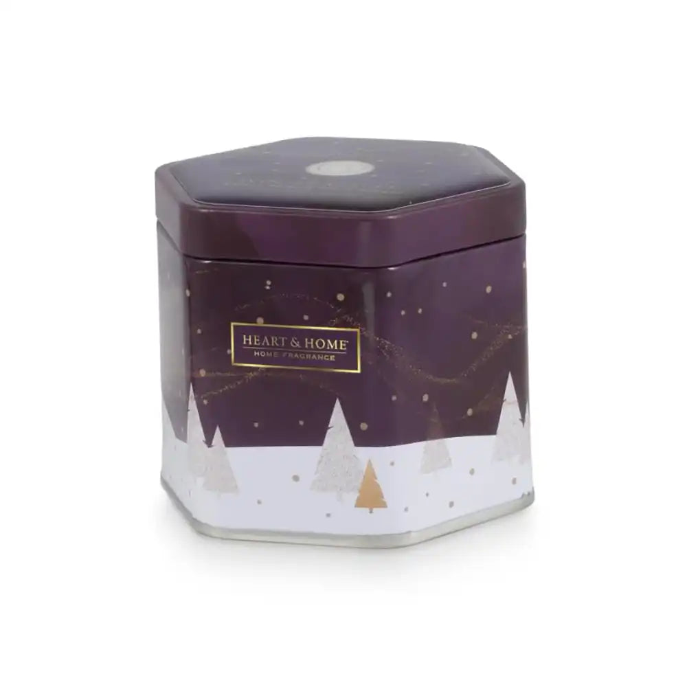 A hexagonal metal tin candle from Heart & Home Fragrance, featuring a dark purple top half with gold stars and a white bottom half with a winter tree pattern.
