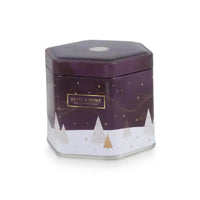 A hexagonal metal tin candle from Heart & Home Fragrance, featuring a dark purple top half with gold stars and a white bottom half with a winter tree pattern.