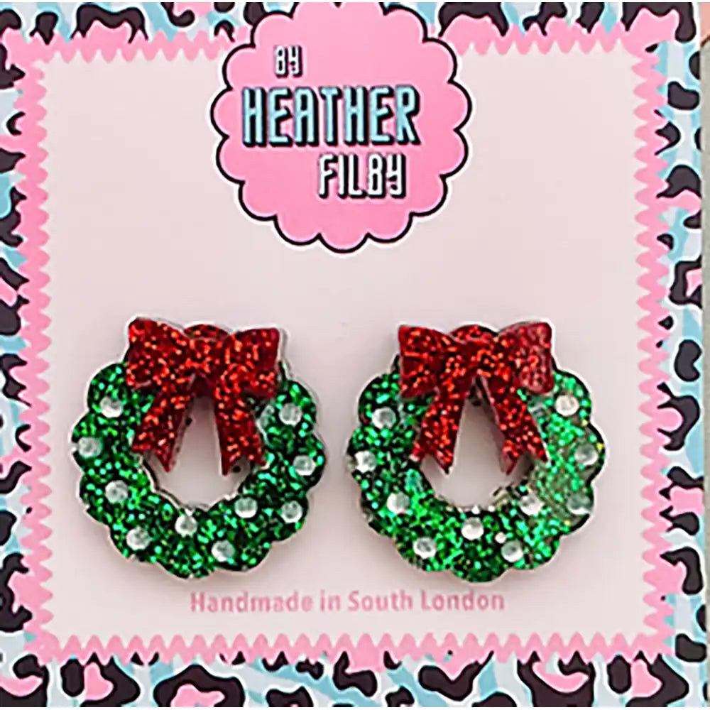 Pair of green wreath earrings with red bows on a colorful card with 'Heather Filby' branding.
