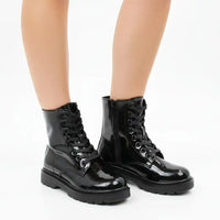 A pair of glossy black patent leather lace-up combat boots with side zippers, shown on a model's feet against a plain white background.