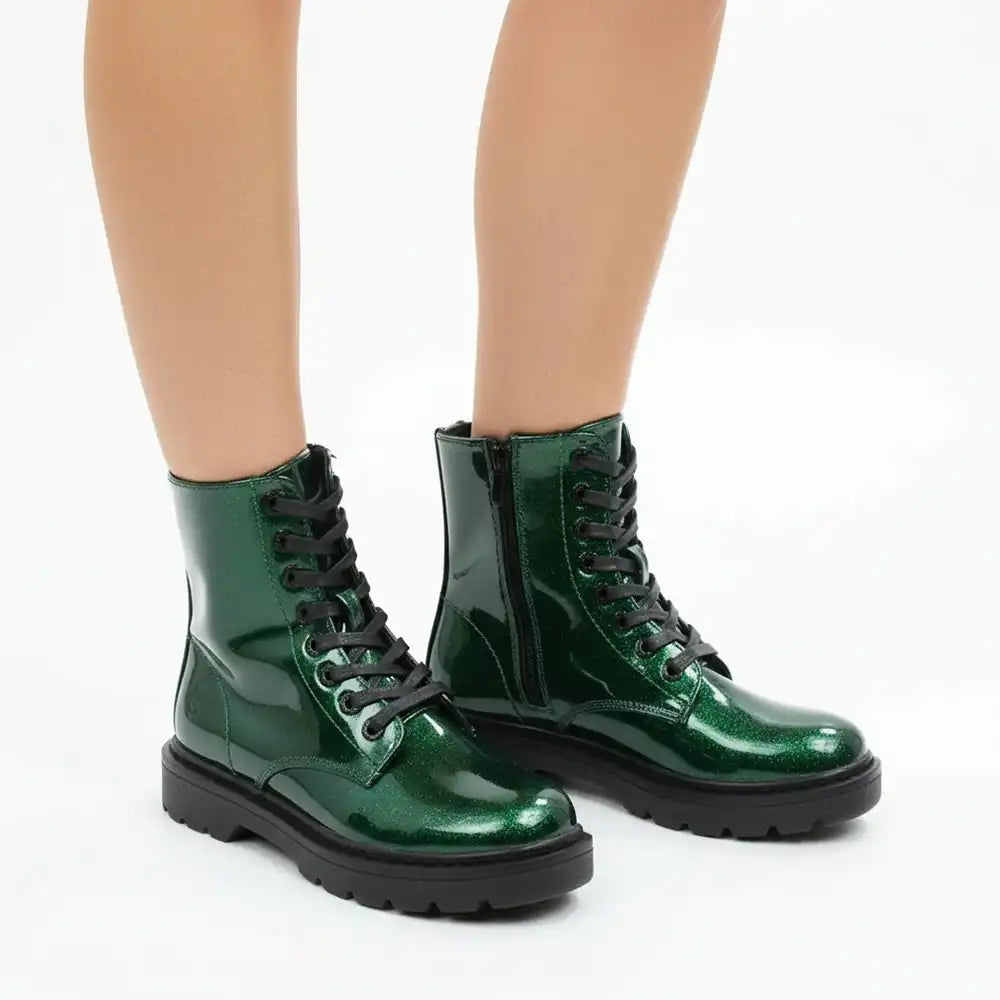 A pair of shiny metallic green lace-up ankle boots with black soles and black laces, shown on a model's feet against a plain white background.