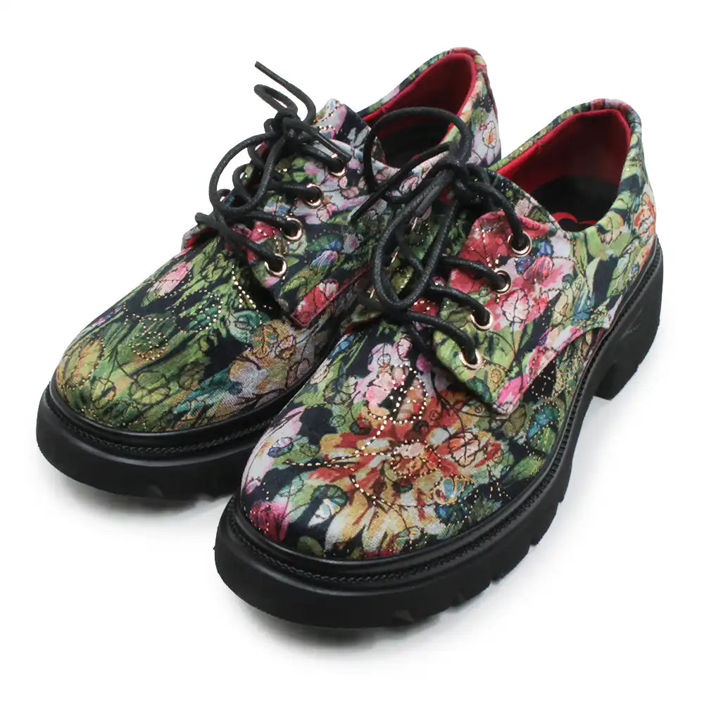 A pair of low-top lace-up shoes with a vibrant, multicolored floral and botanical print on the uppers, black laces, and thick black soles, shown against a plain white background.