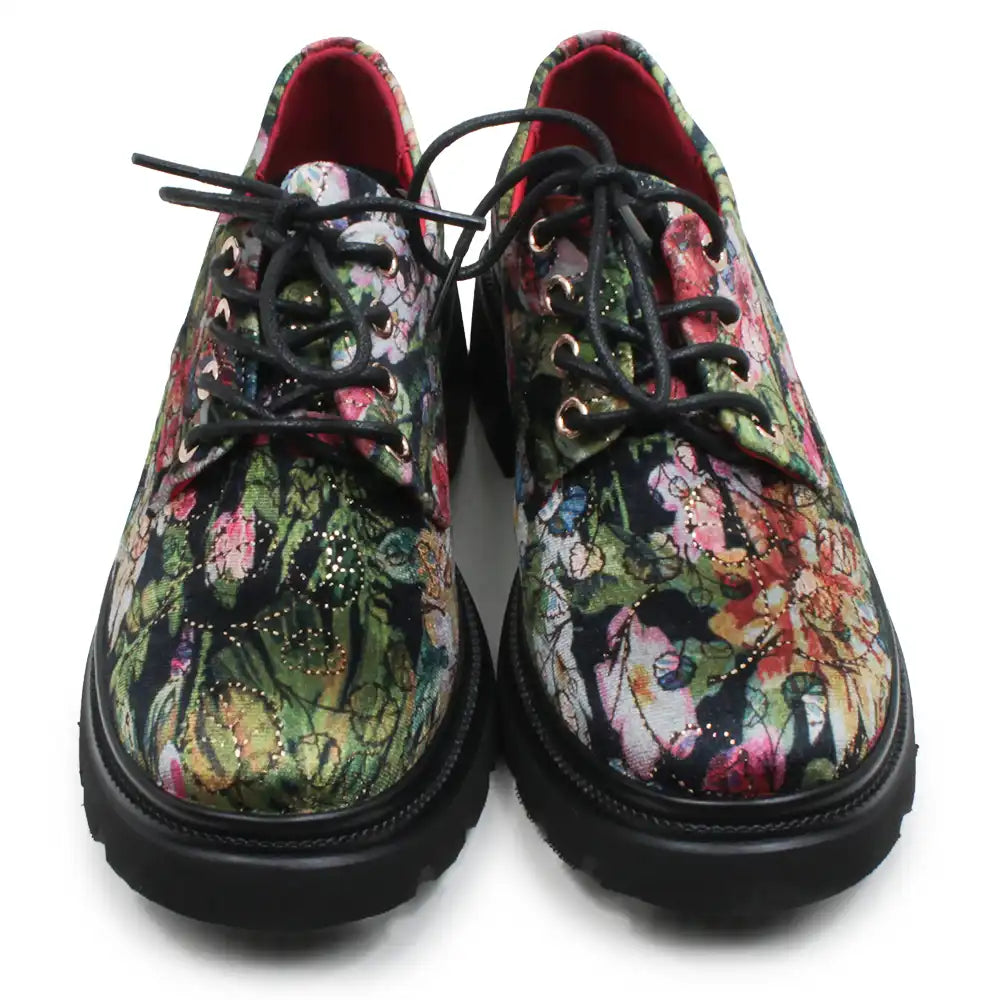 A pair of lace-up oxford-style shoes with thick black soles and black laces, featuring a vibrant, multicolored floral and abstract print on the uppers. The interior lining is red, and the shoes are photographed against a plain white background.