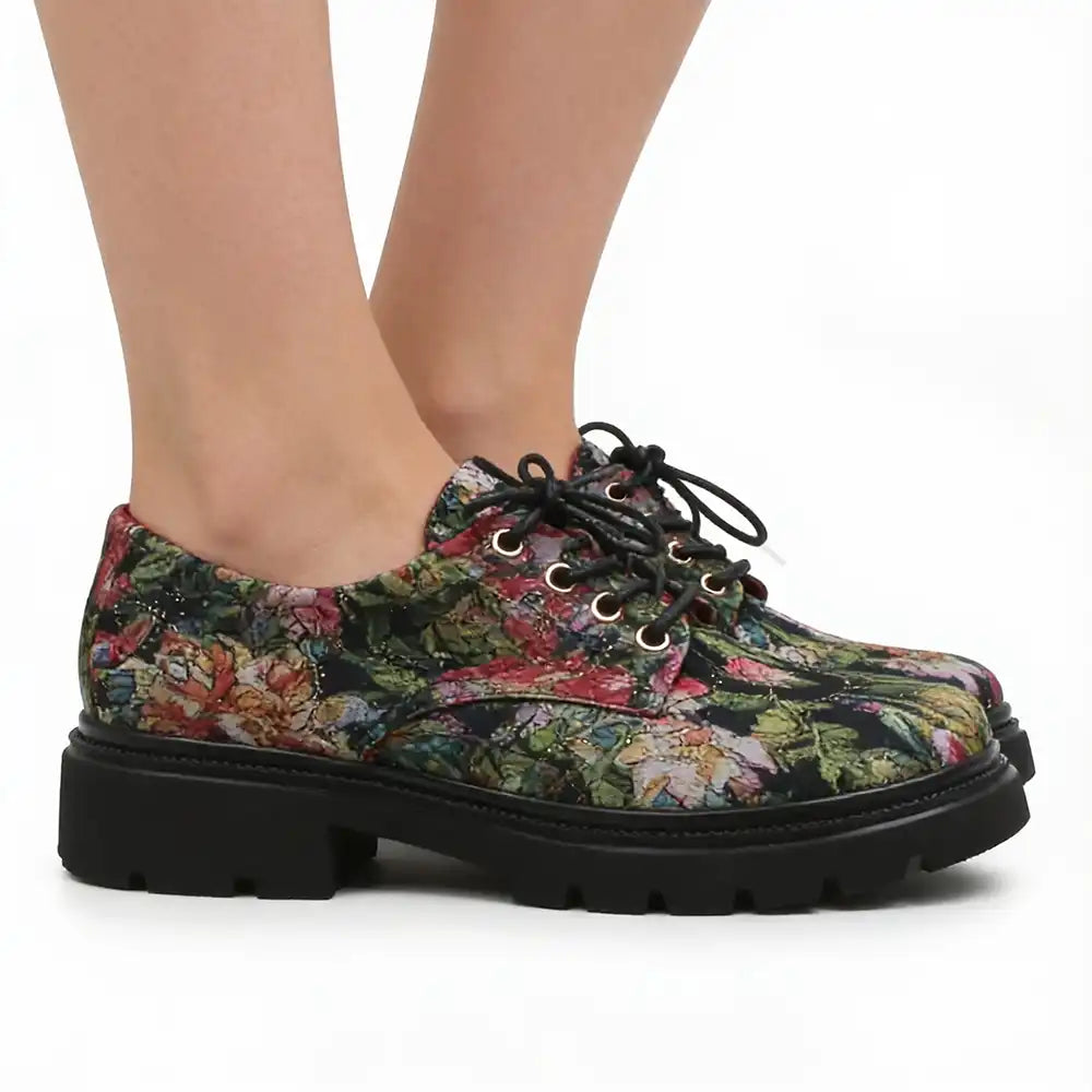 A pair of women's lace-up oxford-style shoes with a dense multicolor floral print and chunky black platform soles, shown on a model's feet against a white background.