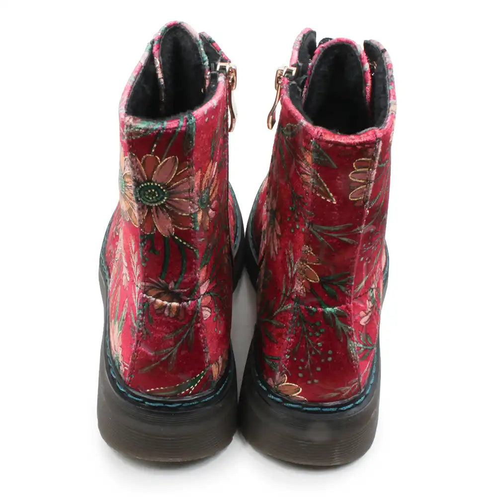 A pair of red velvet ankle boots with an embroidered floral pattern in green, gold, and brown, featuring dark brown soles and side zippers.