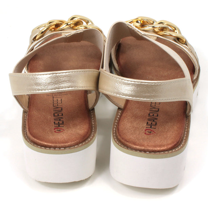 Gold low wedge sandals from Heavenly Feet. Over toes strap and upper foot elasticated strap. Strap around the back of the heel. Chunky gold chain decoration over the toes. Tan coloured footbeds. White low wedge soles with wide deep carved tread. Back view.