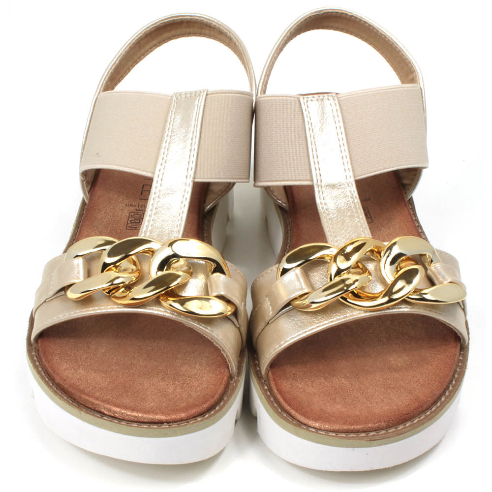 Gold low wedge sandals from Heavenly Feet. Over toes strap and upper foot elasticated strap. Strap around the back of the heel. Chunky gold chain decoration over the toes. Tan coloured footbeds. White low wedge soles with wide deep carved tread. Front view.