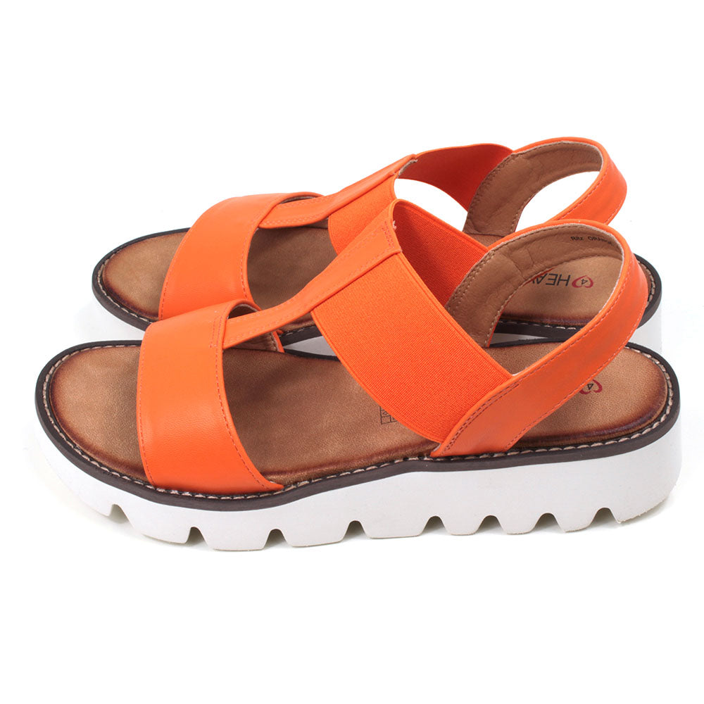 Orange low wedge sandals from Heavenly Feet. Over toes strap and upper foot elasticated strap. Strap around the back of the heel. Tan coloured footbeds. White low wedge soles with wide deep carved tread. Side view.