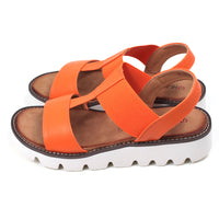 Orange low wedge sandals from Heavenly Feet. Over toes strap and upper foot elasticated strap. Strap around the back of the heel. Tan coloured footbeds. White low wedge soles with wide deep carved tread. Side view.