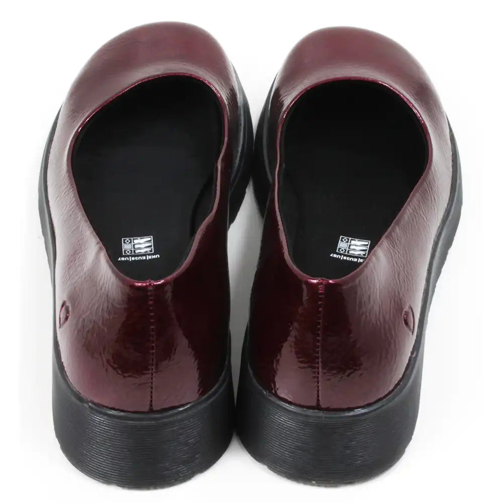 Pair of patent maroon slip on shoes with black low wedge soles. Round toes. Back view.
