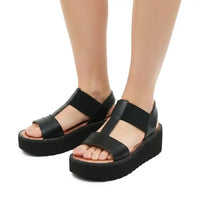 A pair of black platform sandals with wide front straps and ankle straps, shown on a model's feet against a white background.