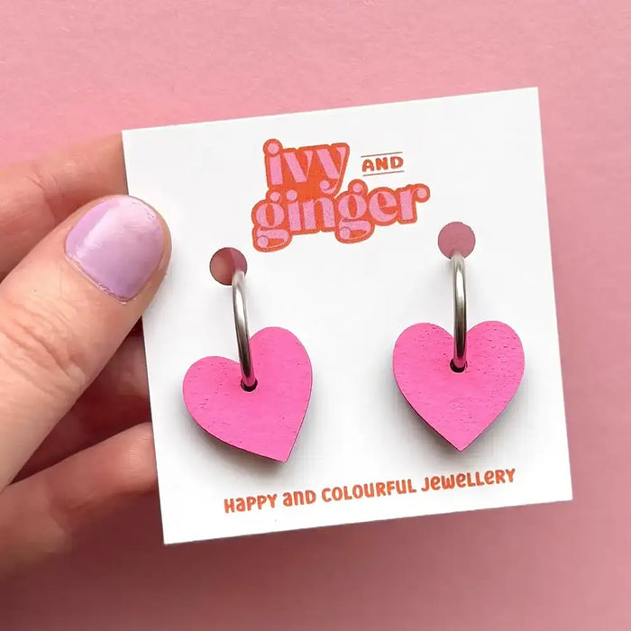 Pink heart-shaped earrings on a 'ivy and ginger' branded card against a pink background.