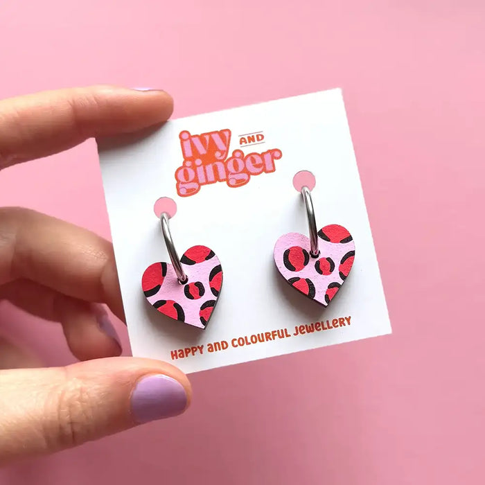Heart-shaped earrings on a 'ivy and ginger' branded card against a pink background