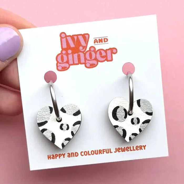 Heart-shaped earrings with black and white pattern on a 'Ivy and Ginger' card against a pink background