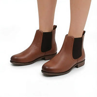 A pair of women's brown leather Chelsea ankle boots with black elastic side panels, shown on a model's feet against a white background.