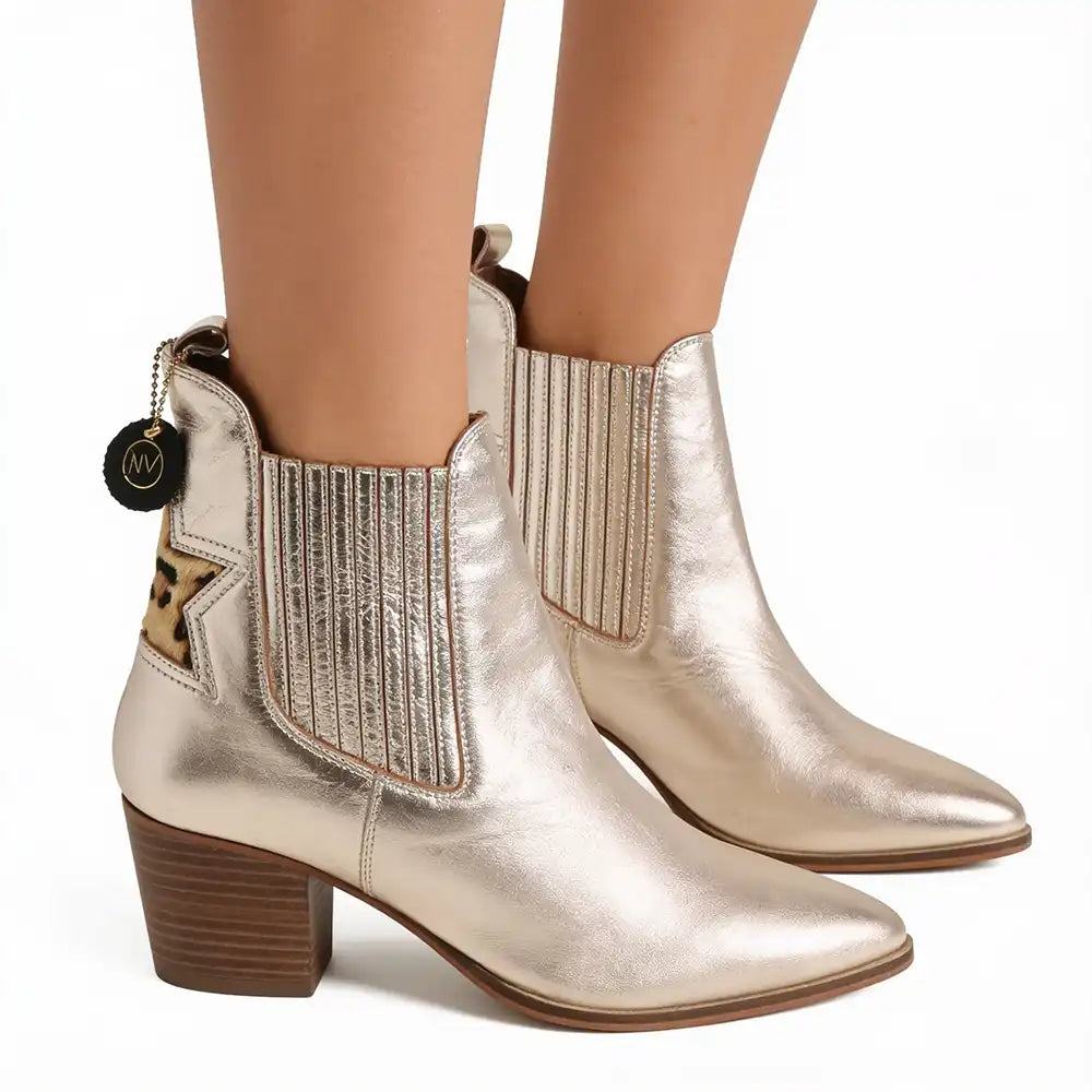 Metallic champagne gold ankle boots with a pointed toe, block heel, and elastic side panels, shown on a model's feet against a white background.