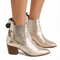 Metallic champagne gold ankle boots with a pointed toe, block heel, and elastic side panels, shown on a model's feet against a white background.