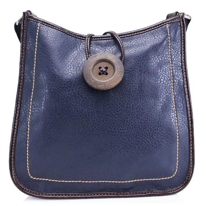 A navy blue pebbled leather shoulder bag with dark brown trim, light beige contrast stitching, and a large round wooden button closure on the front.