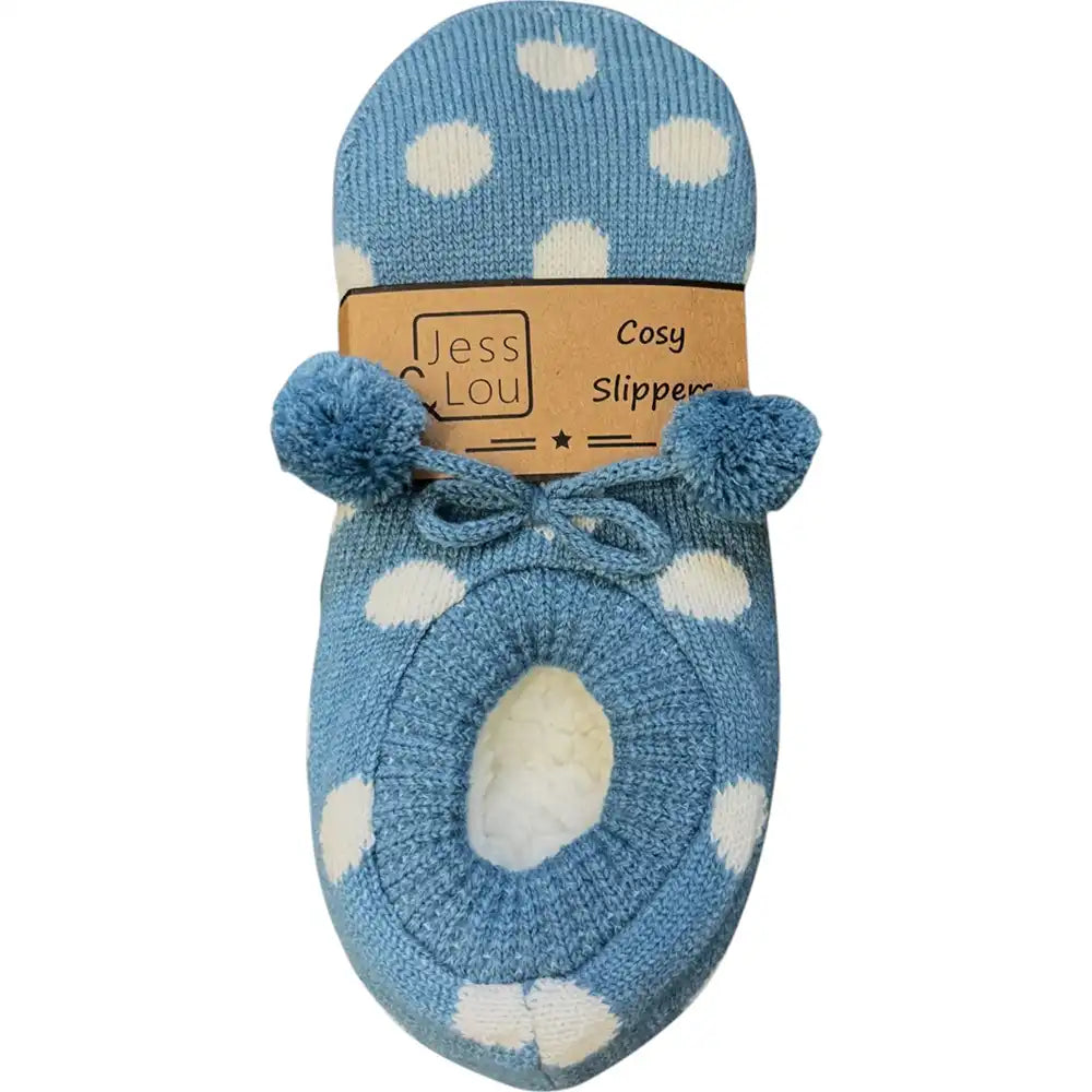 A single blue knit slipper with white polka dots and pom-pom details, shown on a white background with its paper packaging label attached.