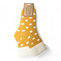 A pair of yellow ankle socks with white polka dots and white fleece cuffs, packaged with a brown paper header card on a white background.