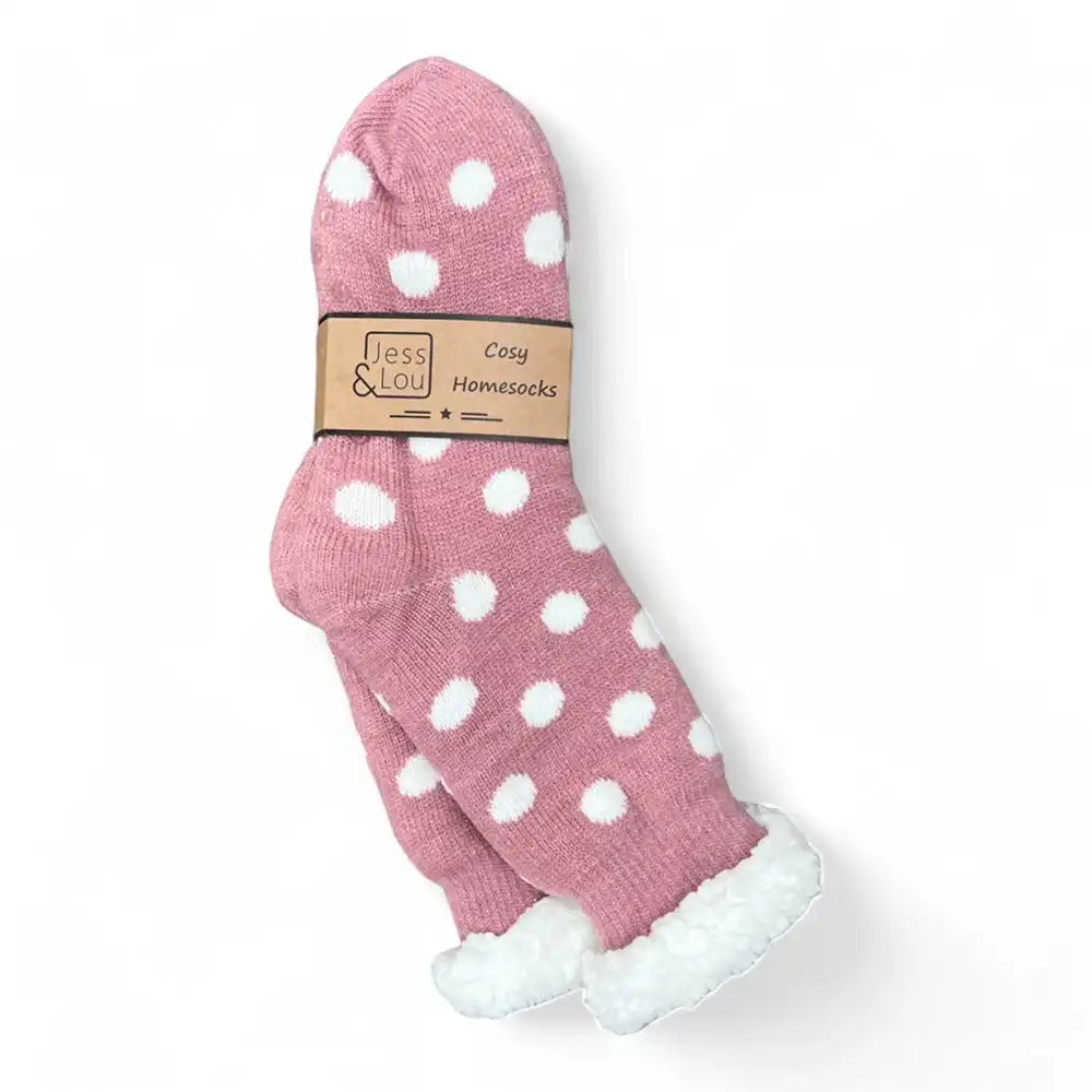 A pair of pink knit home socks with white polka dots and white faux-fur trim at the cuffs, wrapped in a paper band that reads 'Jess & Lou Cosy Home Socks' on a white background.