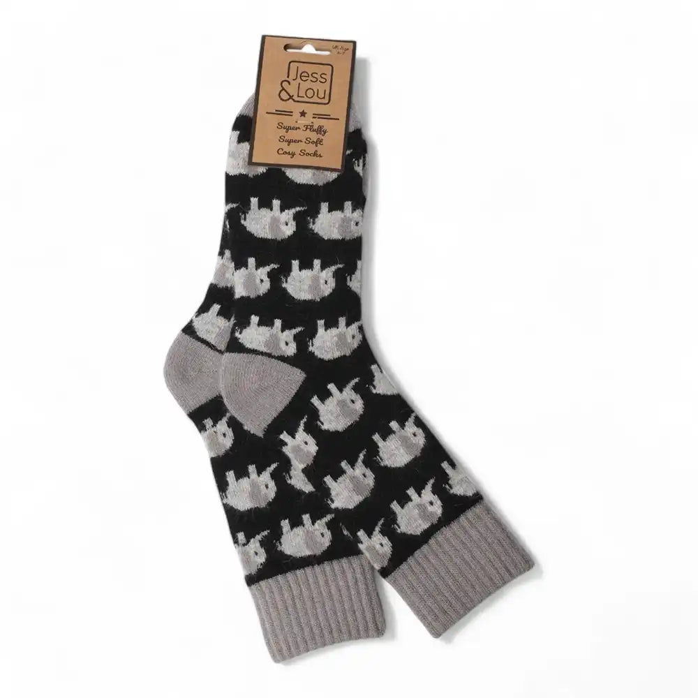 A pair of black crew socks with a repeating pattern of light grey elephants, featuring solid grey heels, toes, and ribbed cuffs. The socks are shown on a white background with a paper brand tag attached.