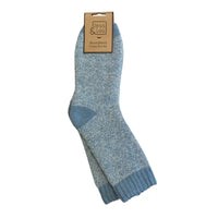 A pair of light blue marled knit socks with a solid medium blue heel and toe, hanging from a brown paper hanger tag that reads 'Jess & Lou Wood Brand Cosy Socks' on a plain white background.