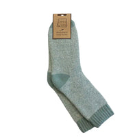 A pair of light blue-green wool blend crew socks with a matching ribbed toe and heel, hanging from a brown paper tag that reads 'Jess Lou Wood Blend Coy Socks' on a solid white background.