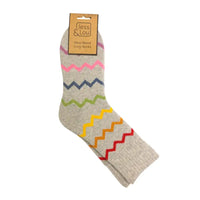 A pair of crew sock in heather grey with colorful zigzag stripes in pink, navy, green, yellow, orange, and red, shown with a cardboard hanger tag reading 'Jess & Lou' on a white background.