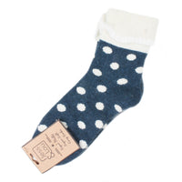 A single navy blue knit sock with white polka dots and a white fuzzy cuff, shown with a paper hangtag on a plain white background.