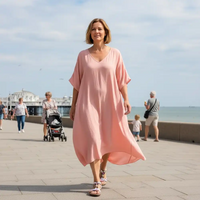 Woman in a pink dress walking on a promenade with people and a stroller in the background.